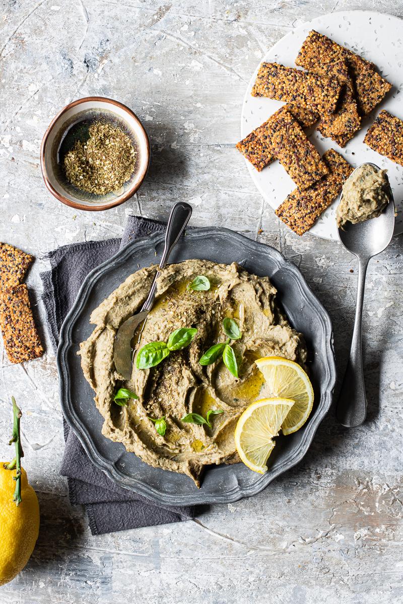 Piatto con dip di carciofi con foglie di basilico e accannto cracker di quinoa senza glutine