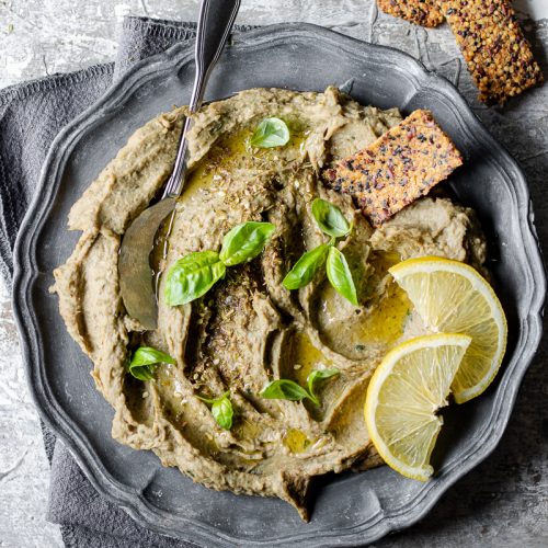 Piatto con dip di carciofi con foglie di basilico e accannto cracker di quinoa senza glutine