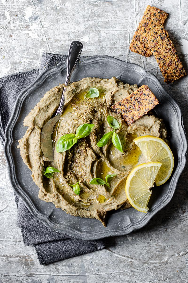 Piatto con dip di carciofi con foglie di basilico e accannto cracker di quinoa senza glutine