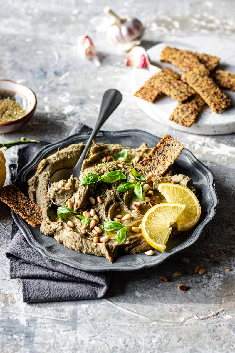 Piatto con dip di carciofi con foglie di basilico e accannto cracker di quinoa senza glutine