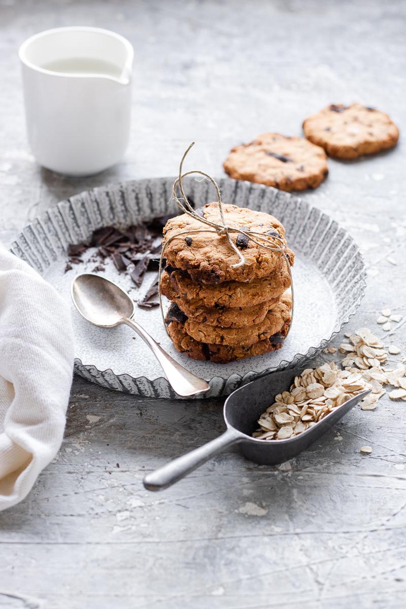 Pila di biscotti all'avena e cioccolato in un vassoio bianco con accanto cioccolato e latte