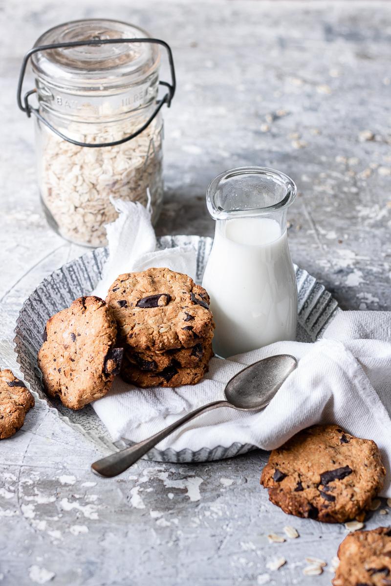 Biscotti all'avena e cioccolato senza glutine e senza burro appoggiati su un vassoio bianco con un bricco di latte