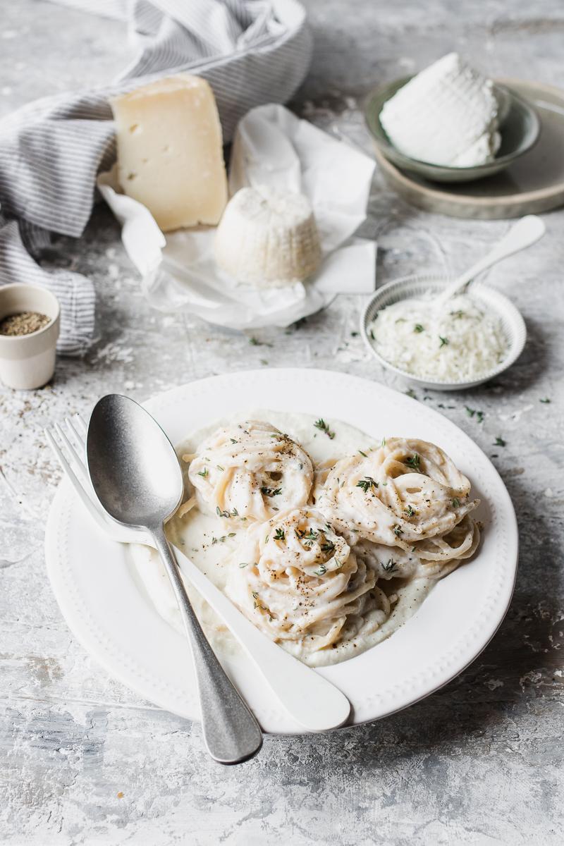 Piatto di alfredo pasta al cavolfiore e pezzi di formaggio di capra nello sfondo