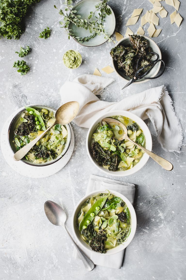 Tre ciotole con minestrone verde con legumi verdure e maltagliati, con cucchiai e foglie sparse, visto dall'alto