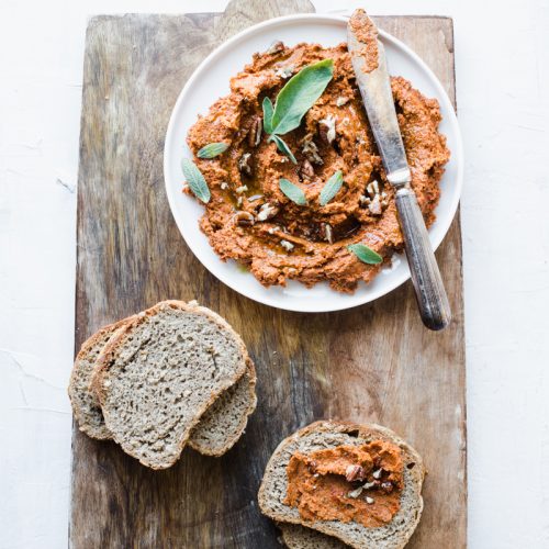 Patè di pomodori secchi vegano con salvia e noci e fette di pane di segale su tagliere