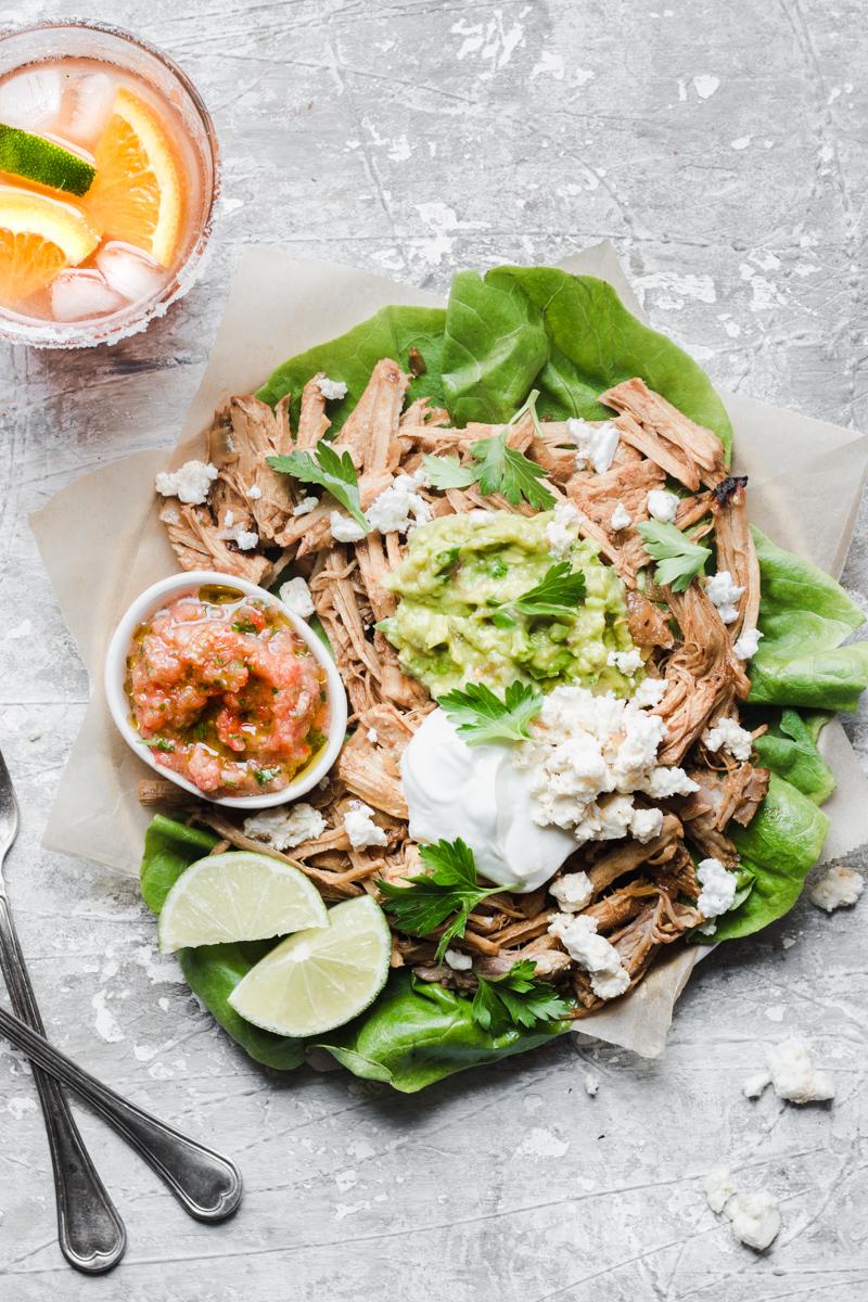 Carnitas plate with guacamole, sauce, queso, greek yogurt and lime with two glass of margaritas