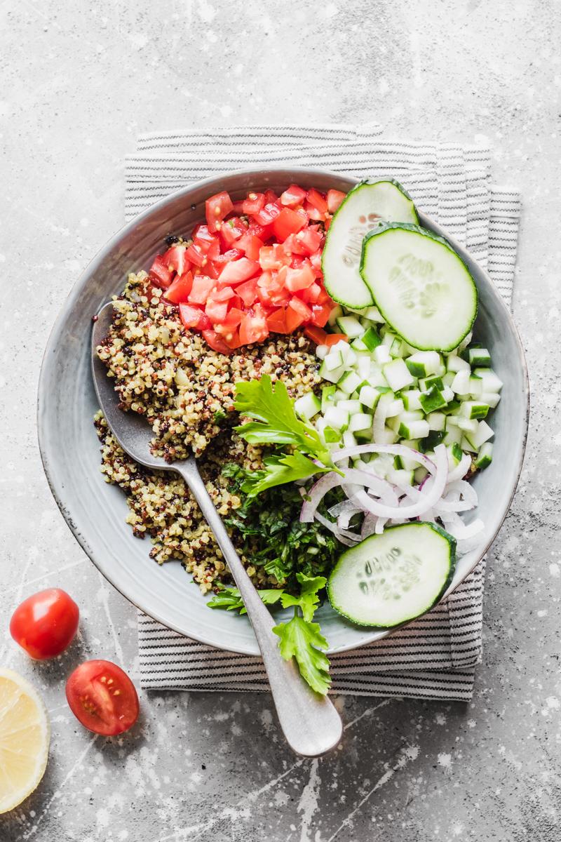 Ciotola con cucchiaio e quinoa tricolore, cetrioli, prezzemolo, pomodoro, cipolla rossa