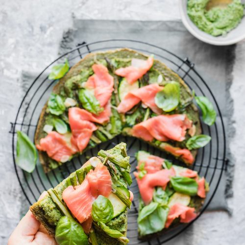 Green socca con salmone affumicato e una mano che ne prende uno spicchio