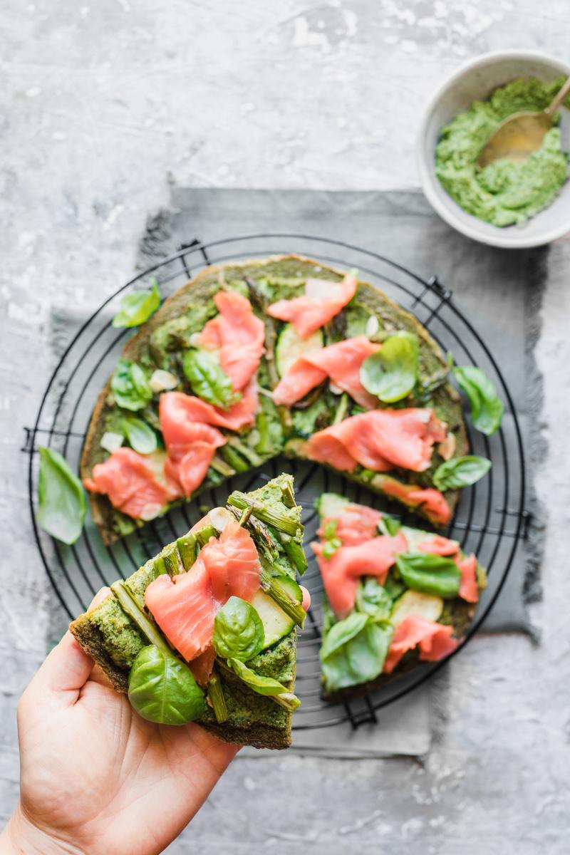 Green socca con salmone affumicato e una mano che ne prende uno spicchio