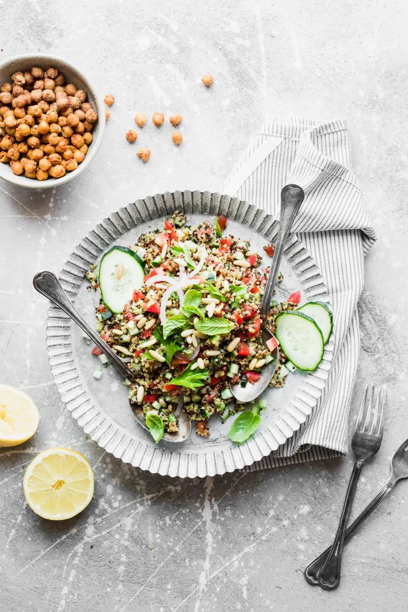 Piatto con due cucchiai e tabbuleh di quinoa tricolore, con ciotola di ceci arrosto