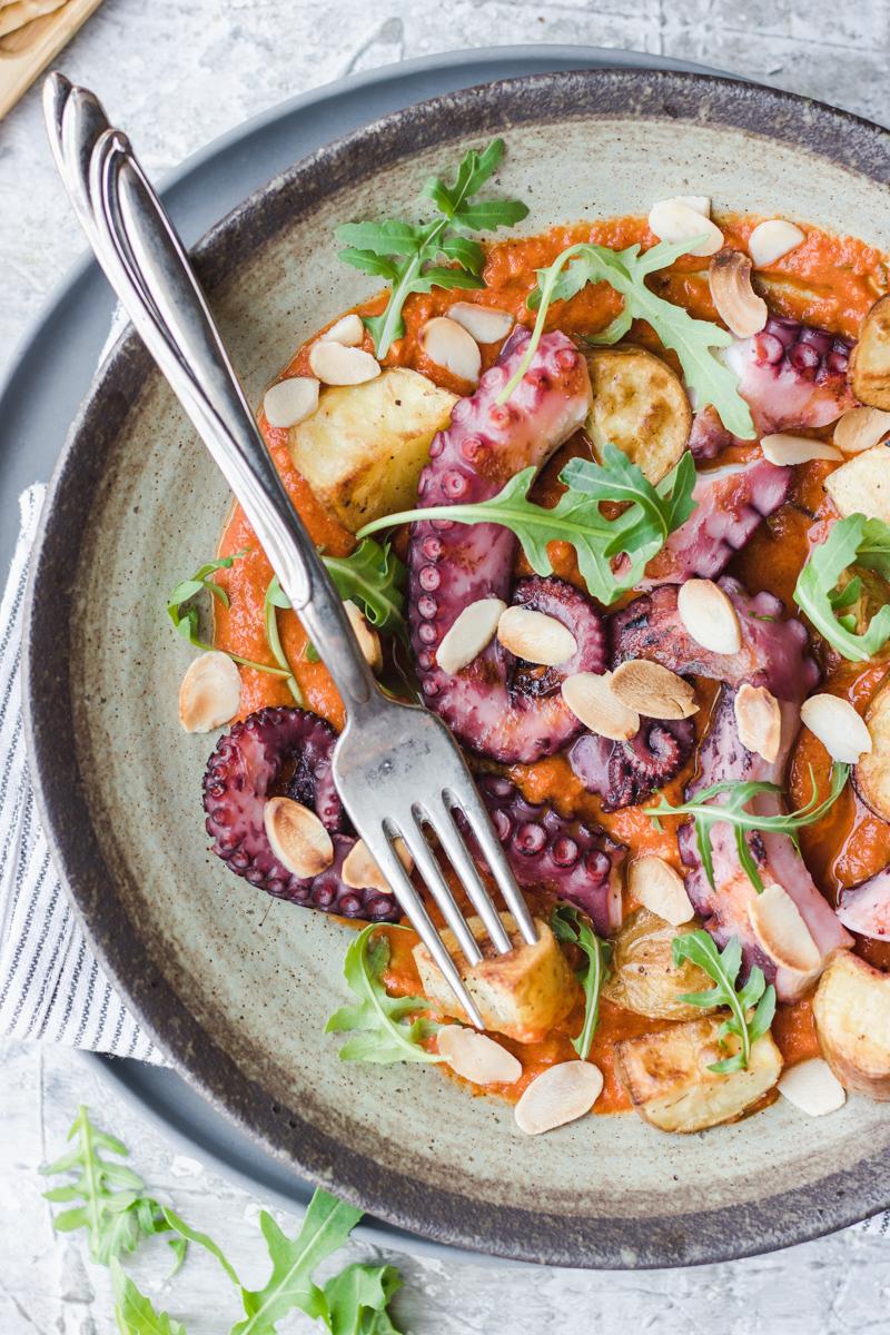 Piatto di polpo con patate arrosto, rucola e salsa romesco con forchetta