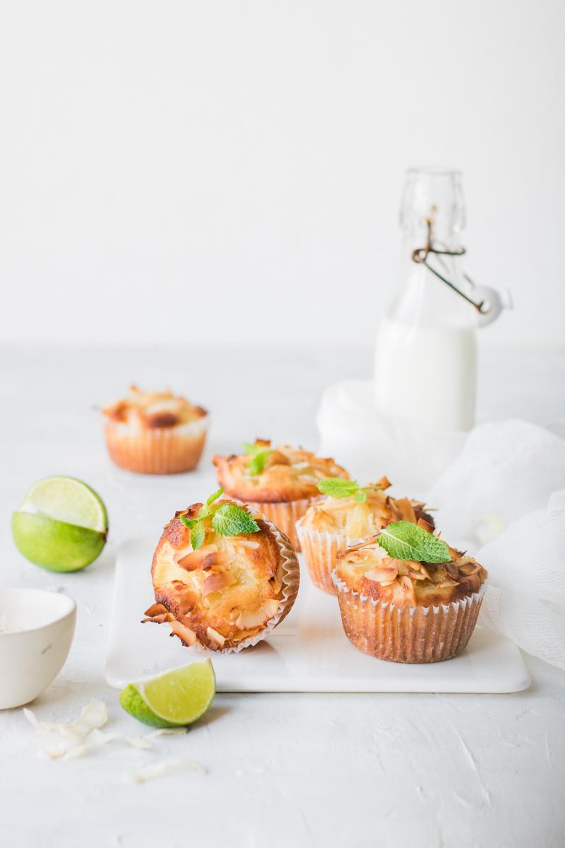 Muffin al cocco e ananas su un tagliere di ceramica bianca con un lime tagliato e bottiglia di lette sullo sfondo