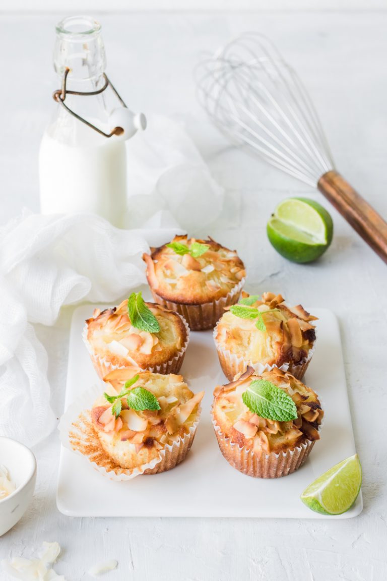 Muffin piña colada su un tagliere di ceramica bianca con un lime tagliato e bottiglia di lette sullo sfondo