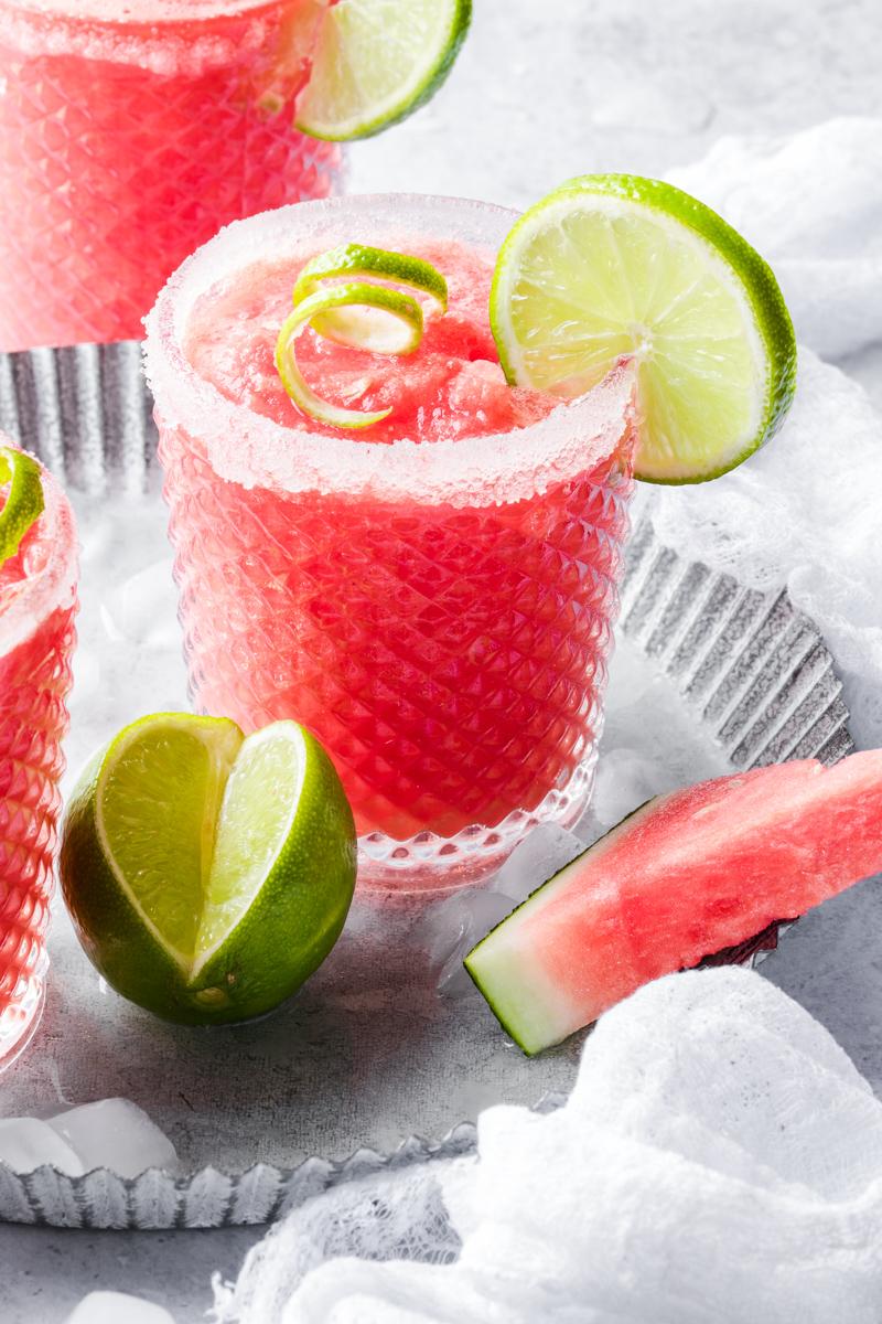 Un bicchiere con drink all'anguria con fetta di lime, lime aperto a fianco e fetta di anguria