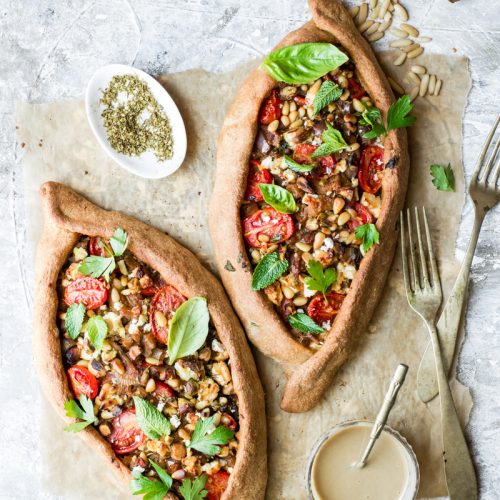 Foglio di carta da forno con due pizze turche con pomodorini, ciotolina con origano secco e posate