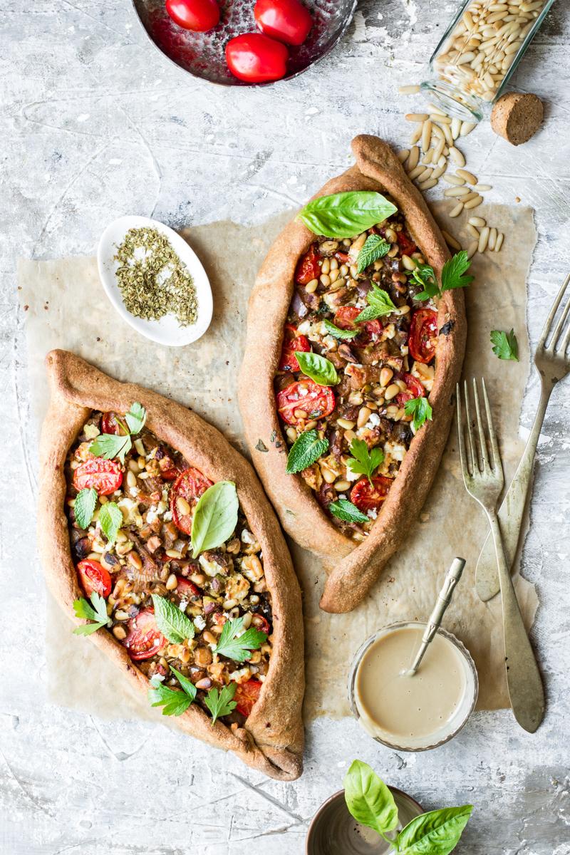 Foglio di carta da forno con due pizze turche con pomodorini, ciotolina con origano secco e posate