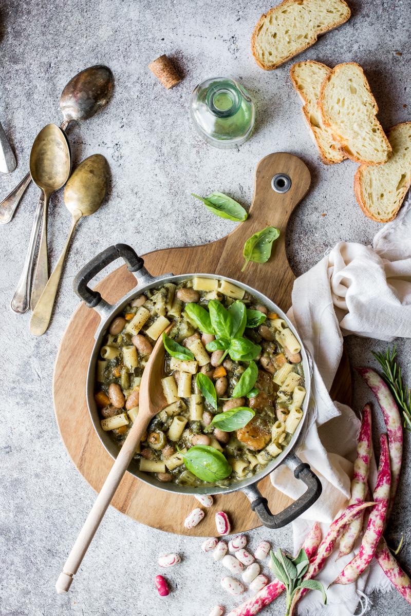 pentola di minestrone con basilico su tagliere con strofinaccio e cucchiai