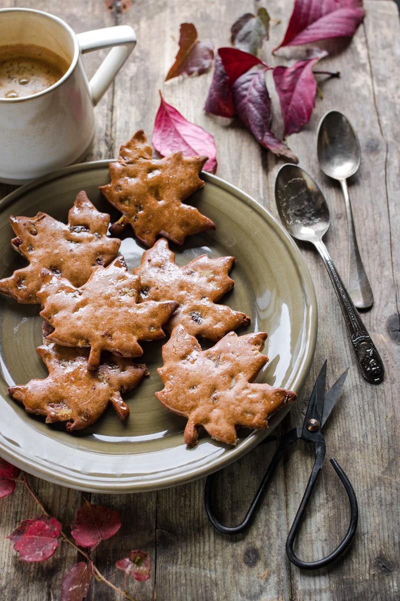 biscotti di farina di castagne a forma di foglia su un piatto con attorno foglie e una tazza di caffè