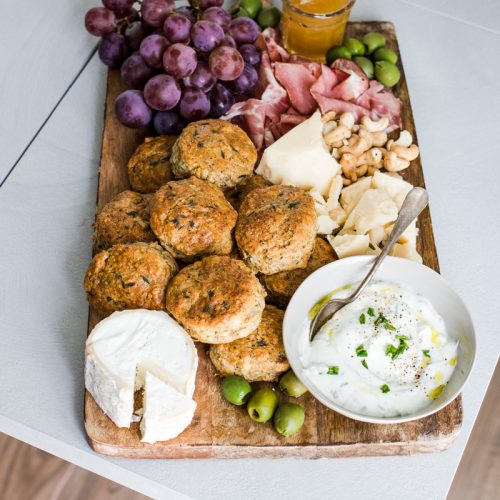 tagliere con scones salati salumi, formaggi, uva e ciotola con panna acida