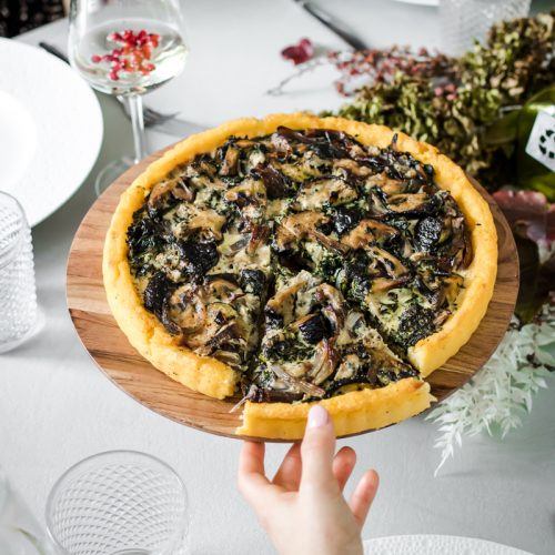 alzatina con tart di polenta ripiena di verdure e una mano che ne prende una fetta