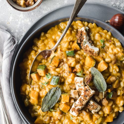 Piatto di orzotto alla zucca e castangne con primosale e foglie di salvia con cucchiaio infilato nel piatto