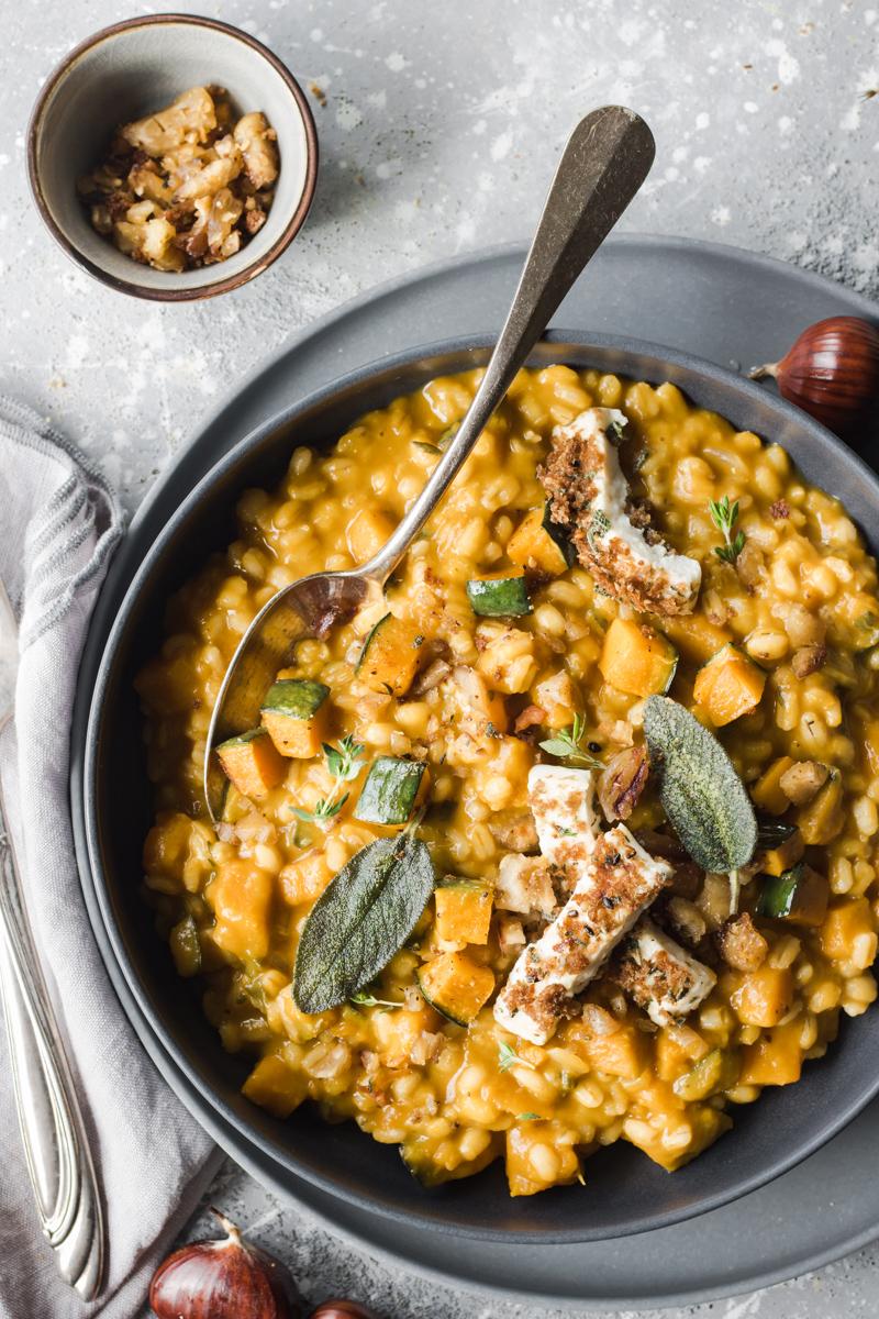 Piatto di orzotto alla zucca e castangne con primosale e foglie di salvia con cucchiaio infilato nel piatto