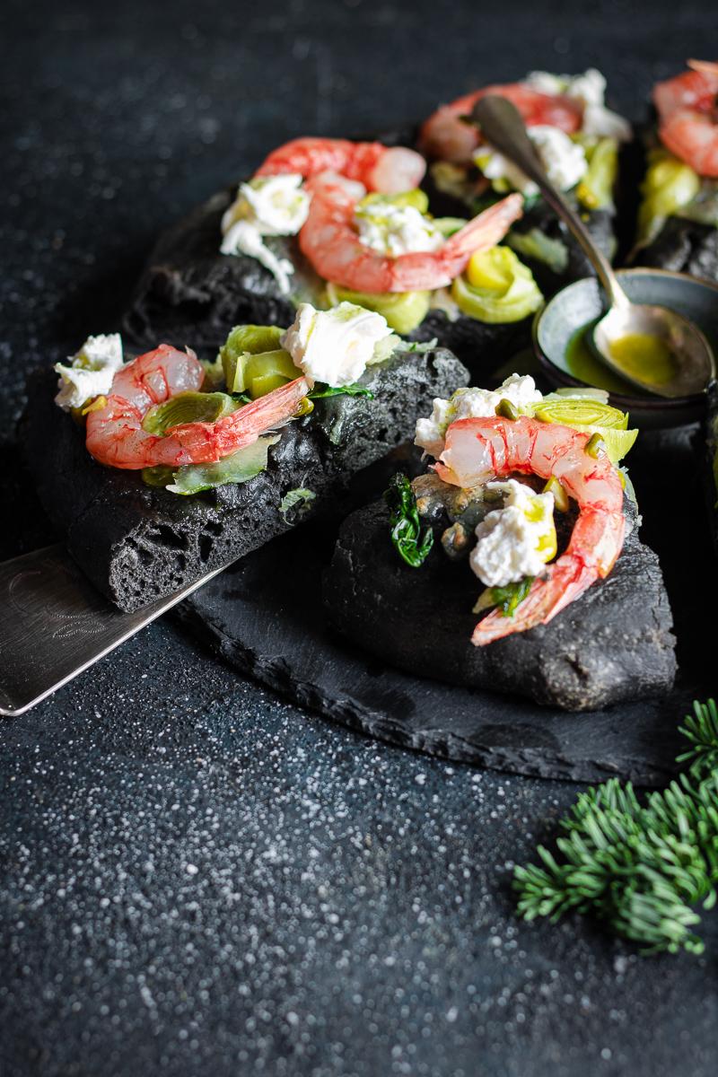 Paletta che preleva una fetta di focaccia al nero di seppia, gamberi rossi e burrata