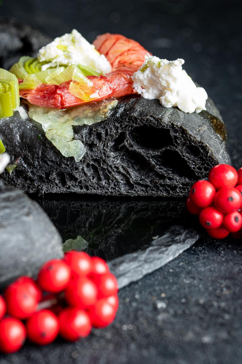 alveolatura di una fetta di focaccia al nero di seppia con gamberi rossi e porri