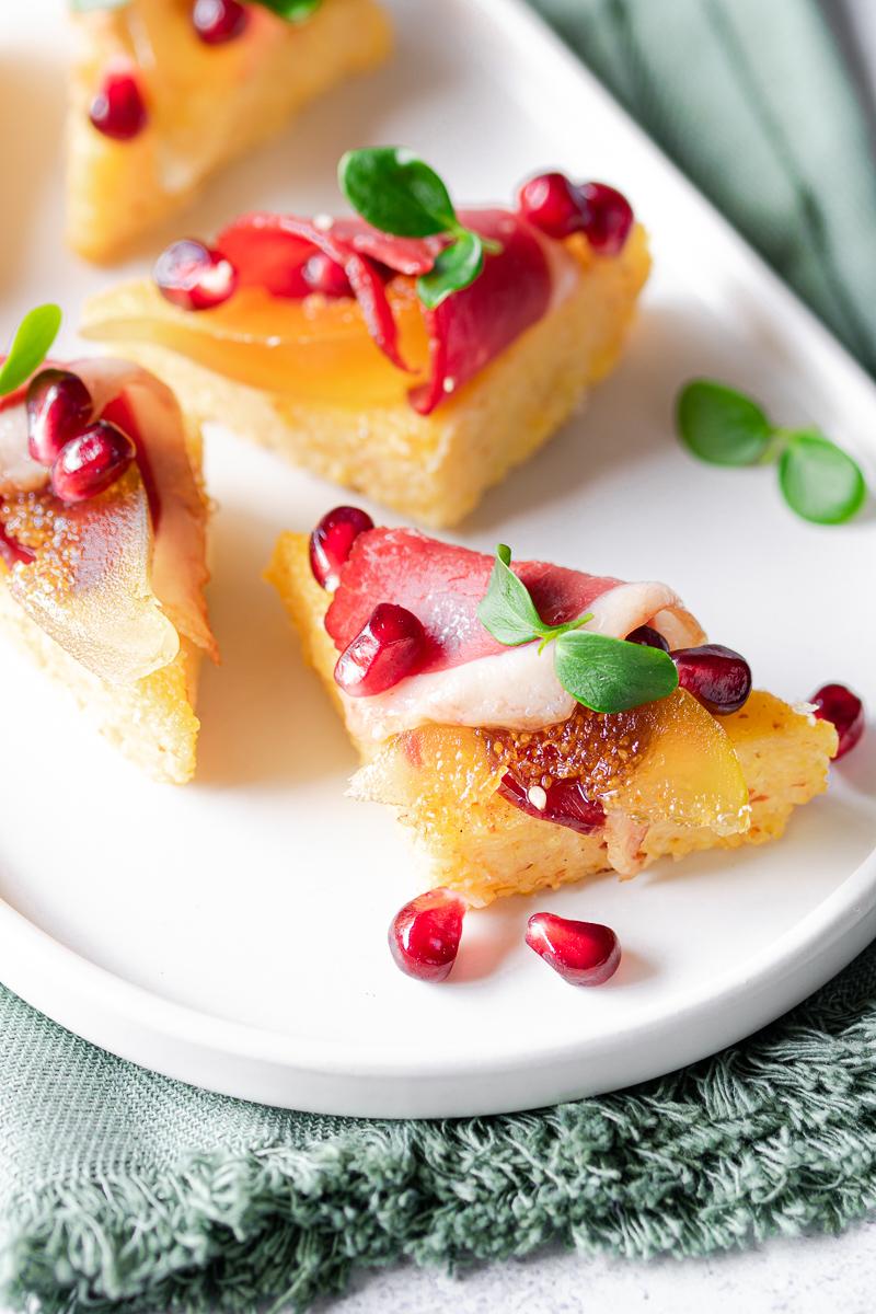 Foto macro di uno stuzzichino di polenta con speck d'anatra, chicchi di melograno e germogli