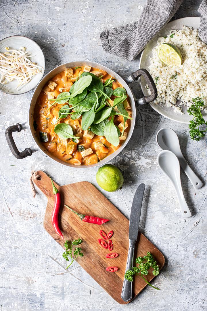 tagliere piccolo di legno con lime coltello e peperoncini e tegame con thai curry vegano con spinaci e riso di cavolfiore