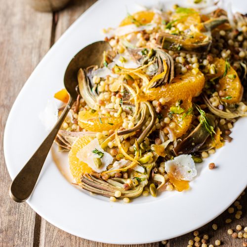 Vassoio bianco con insalata di fregola con carciofi, arancia, bottarga, pecorino e pistacchi